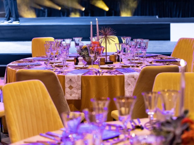 Round table with gold table cloth, gold charger plate, navy menu, and gold and white napkins.