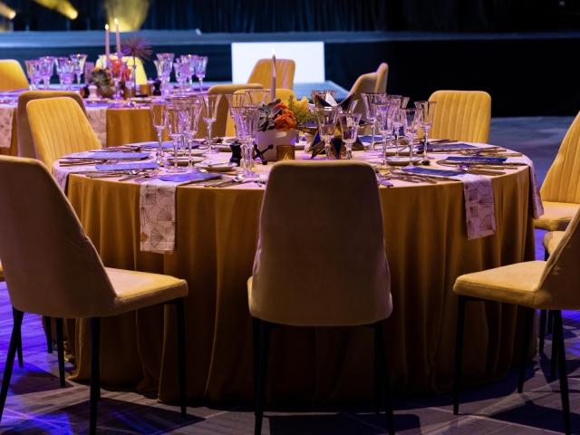 Round table with gold table cloth, gold charger plate, navy menu, and gold and white napkins.