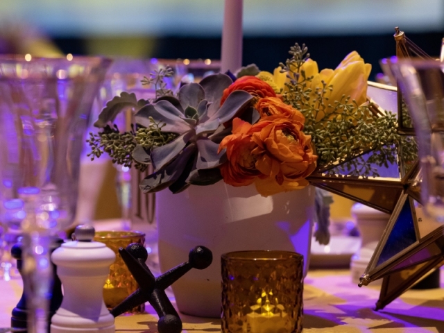 Close up of floral centerpiece with a variety of flowers, colors, and candle in center.