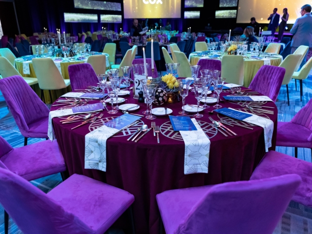 Round table with maroon table cloth, velvet chairs,  and silver table setting with menu.