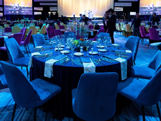 Round table with navy table cloth, gold charger plate, navy menu, and gold and white napkins.