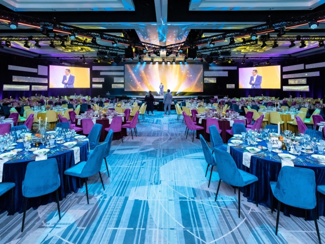 A view of the executive forum gala with blue, red, and gold tables and stage.