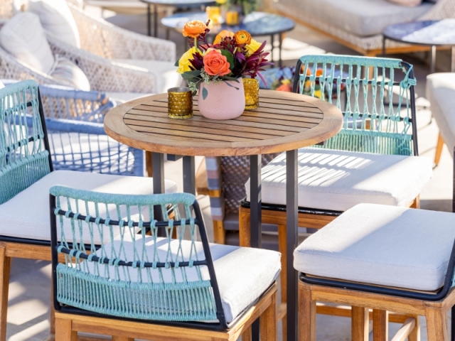 Wooden table with chairs including blue string backing and a floral centerpiece consisting of orange and yellow flowers.