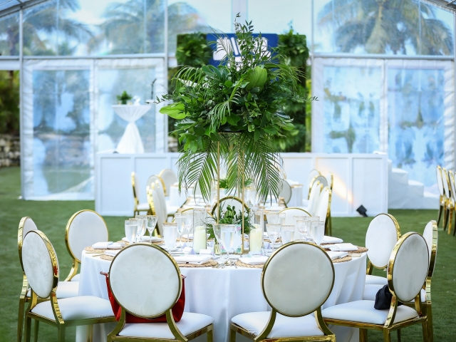 Round table with white table cloth, white and gold chairs, table settings, large foilage centerpiece and candles for incentive trip dinner.