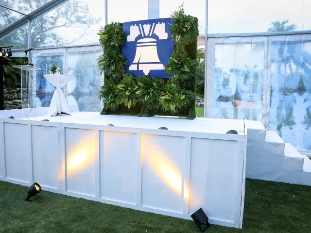 A white stage with foilage and client logo backdrop with podium and mic.