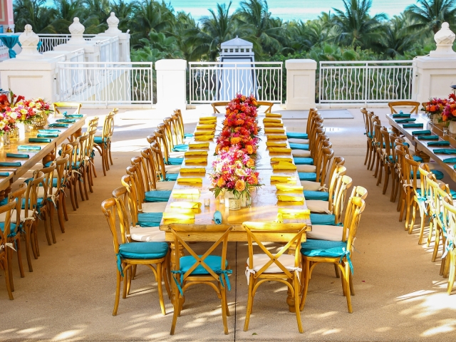 Welcome reception long wooden tables with teal place settings and floral arrangements.