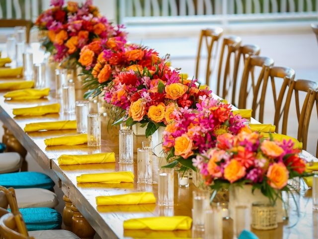 Up close of the table setting with yellow napkins, teal chairs, and floral centerpieces.