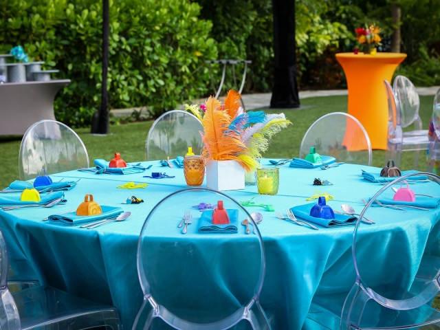 Junkanoo party round table with blue table cloth, blue napkins, multi color bells on tables  