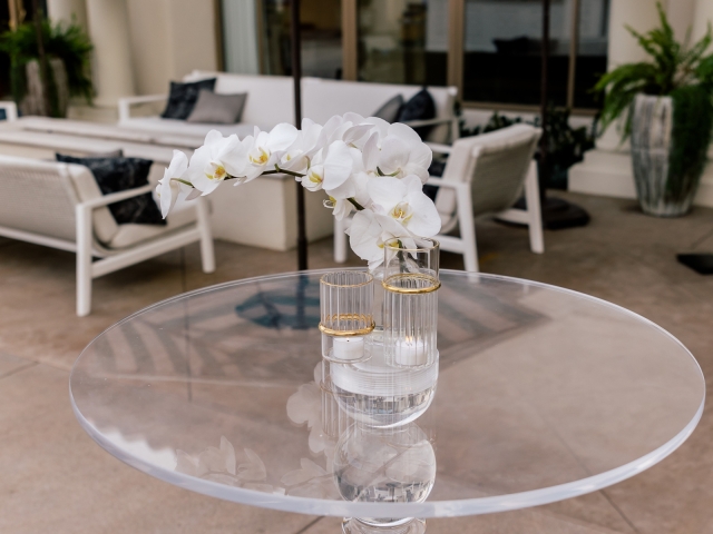 White orchid with white candles on a clear glass table.