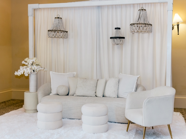 White party lounge area with white couch, chairs, pillows, and chandeliers.