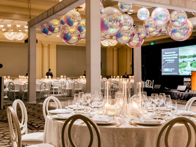 A view of a white party event with round and rectangular tables and silver ball decor hanging from the ceiling.