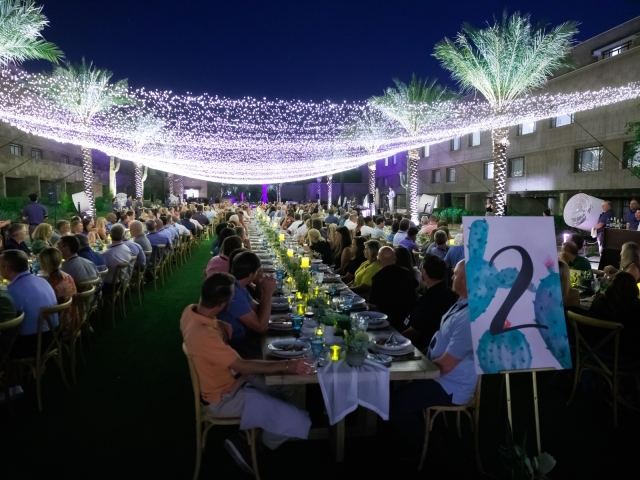 A nighttime view of the king tables filled with guests with hanging lights.