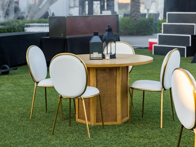 Small wooden round table with white and cold chairs and candle centerpiece display.