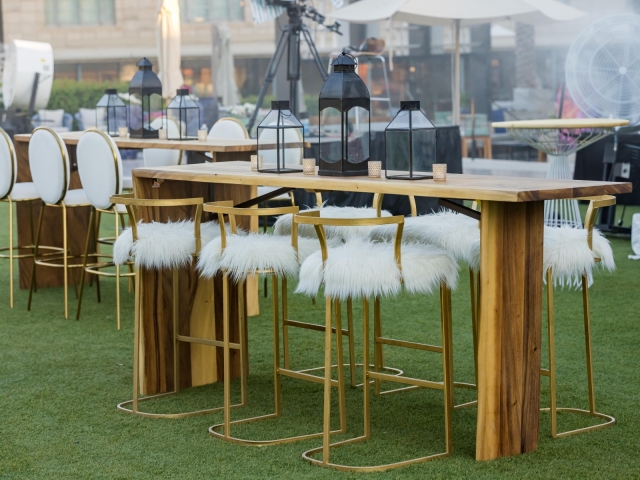 High top  wooden table with gold and white chairs with feather cushions and candle centerpiece display.