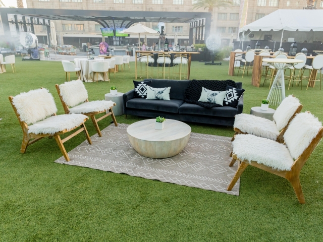 Lounge area at dessert reception with black couch and black and white patterned pillows, wooden lounge chairs with featured cushions, and a brown and white carpeted area.