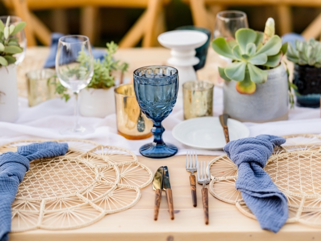 King table setting with bamboo like charger and blue napkin and glasses.