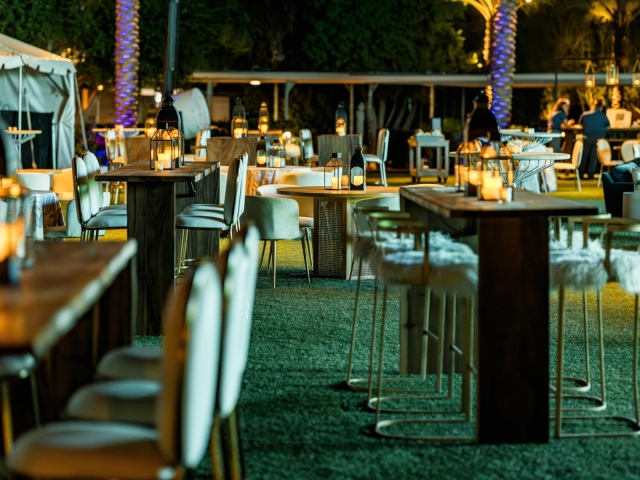 A night time view of tables and chairs at a dessert reception with lit candles.