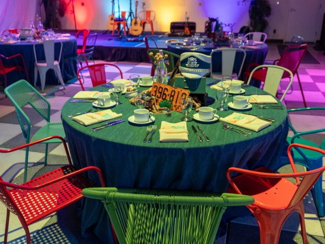 A view of the table at an Austin-themed event with blue table cloth, different style chairs and Austin-themed centerpiece.