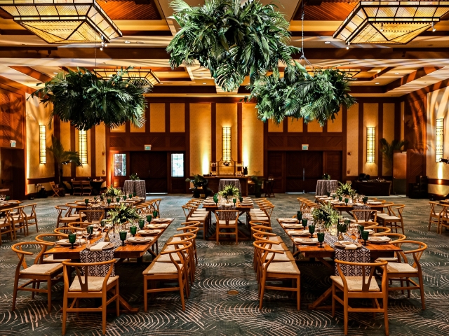 A view of an awards dinner at Four Seasons in Hawaii with wooden tables and green foliage plants.