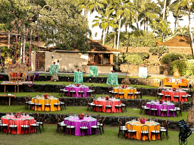 Outdoor venue with 9 tables and yellow, purple, and coral tablecloths.