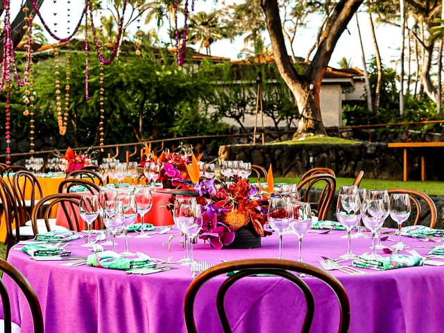 Round table with purple tablecloth and black chairs with floral centerpiece.