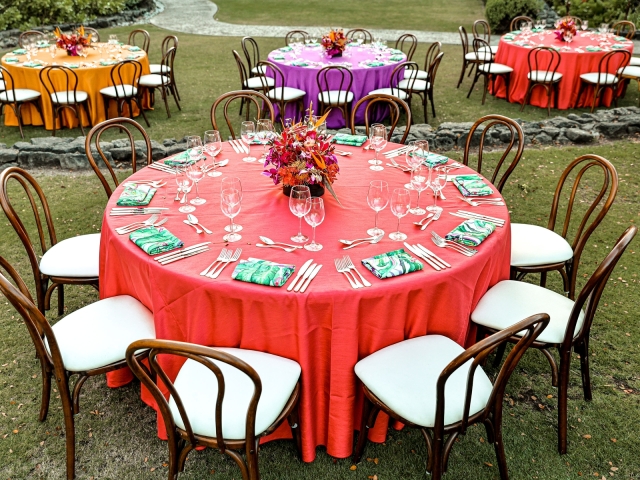 Round table with coral  tablecloth and black chairs with floral centerpiece.