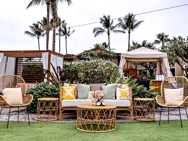 A lounge area with wicker couch, chairs, and tables with a variety of pillows.