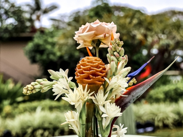 A centerpiece with Hawaiian flowers and stones in small white pot.