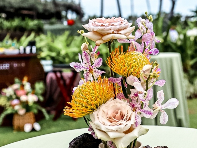 A centerpiece with Hawaiian flowers and stones in small white pot.