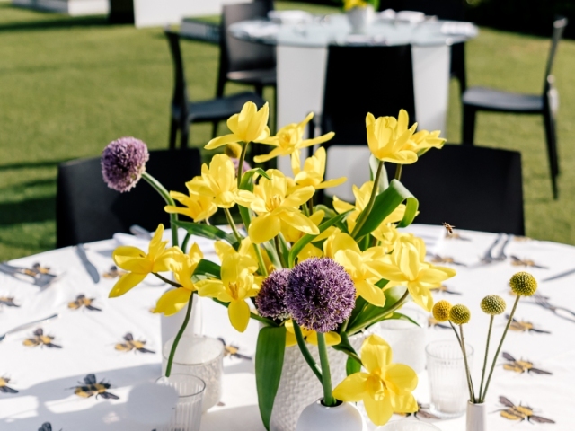 Close up of purple and yellow floral centerpiece on a bee tablecloth.