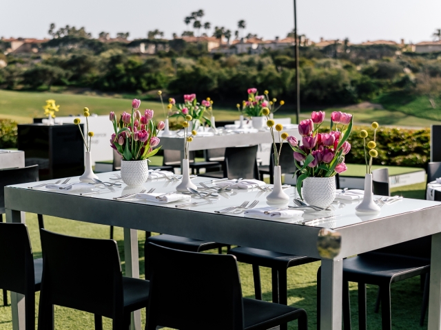 Table arrangement with grey table, black chairs, and floral centerpieces.