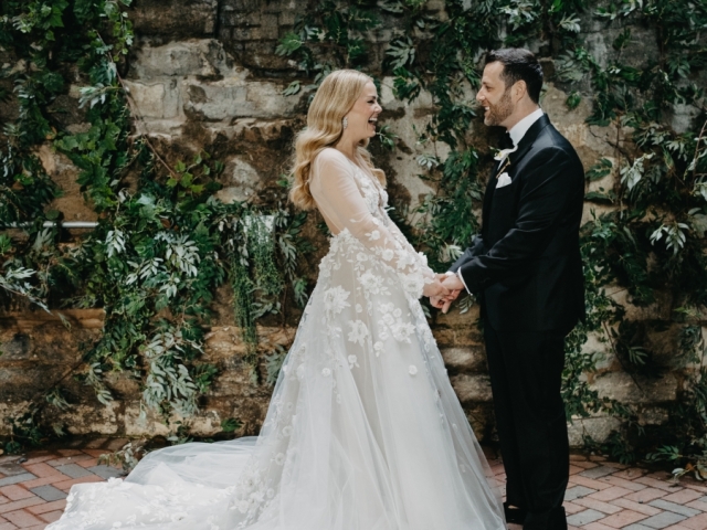 Bride and groom smiling and looking at each other in front of stone wall