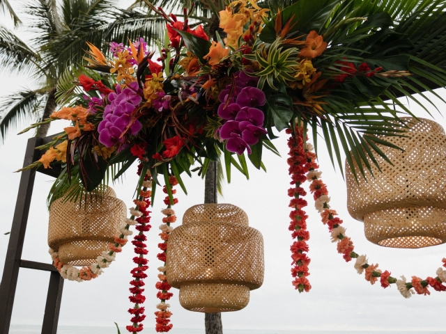 Floral display with bright Hawaiian flowers, hanging leis and wicker lights.