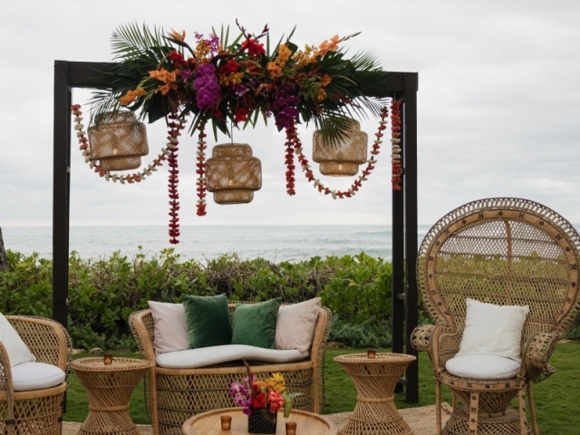 Wicker style couch, chairs, and tables with a floral archway overlooking the ocean.