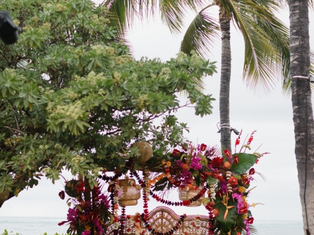 A large wicker chair at an outdoor event overlooking the ocean with Hawaiian flowers surrounding it.