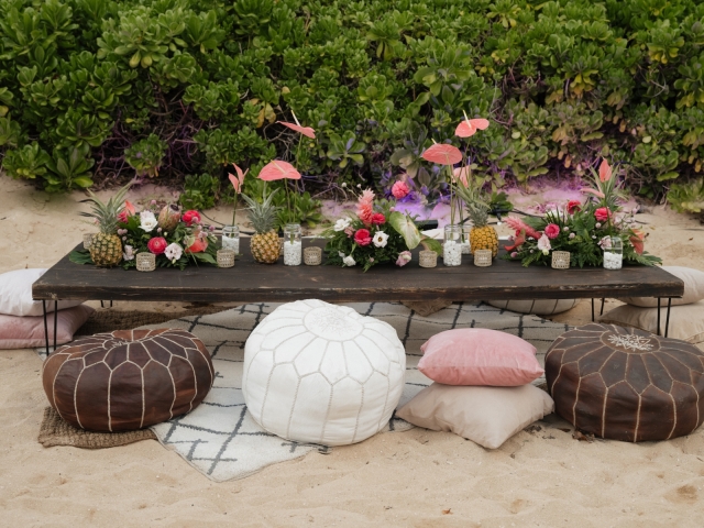 Low wooden table on the beach in Hawaii with pillow chairs.