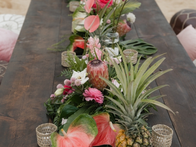 Low top long table on the beach with a floral centerpiece.