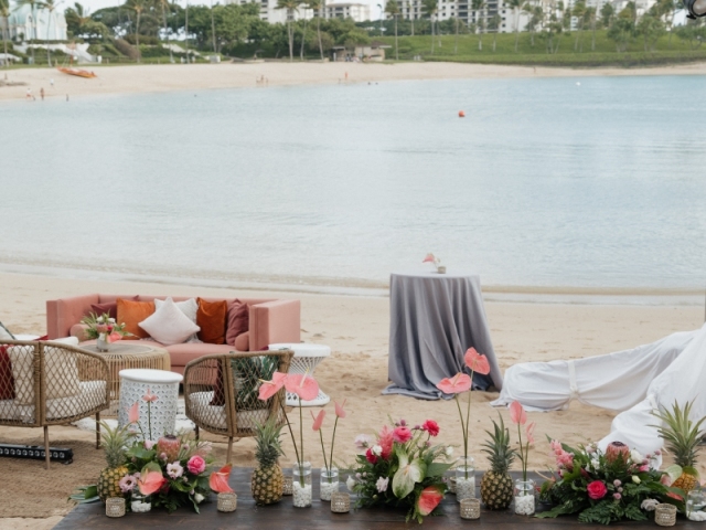 Low top long table on the beach with a floral centerpiece and cushion seats.