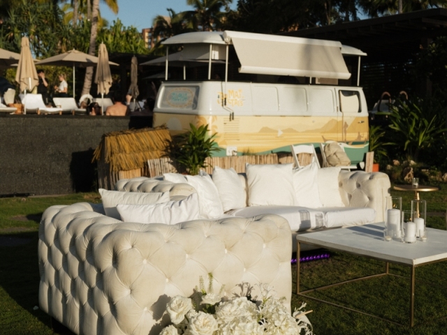 Lounge area with white couch and chair and white table with white candle centerpieces and white hydrangeas on the ground.