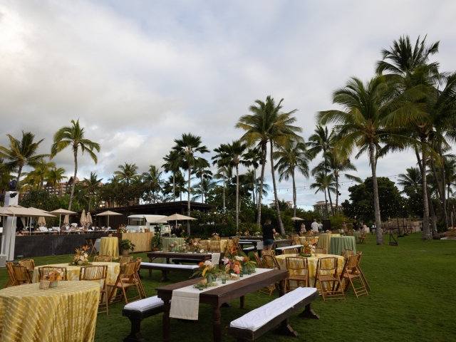 Outdoor event space with a variety of style tables, wooden chairs, overlooking the ocean with palm trees.