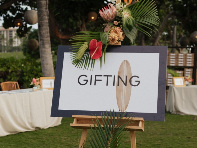 Gifting sign display on an easel with topical flowers.