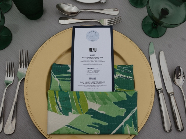 Table setting with gold charger plate, printed menu, tropical napkins, and silverware.