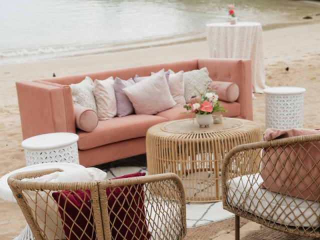 Coral couch with wicker chairs on the beach in Hawaii.