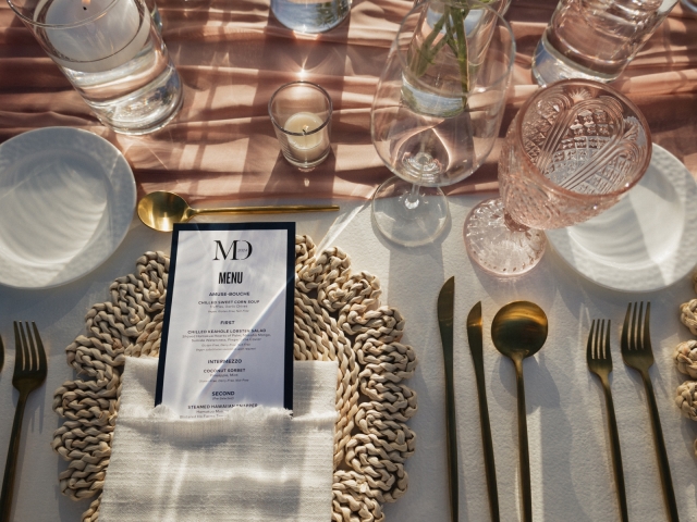 A place setting including charger plate, menu, and gold silverware.